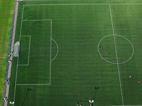 Aerial view of a football pitch with players on the field, green artificial turf, white markings, and surrounding fence in Studley, England, United Kingdom.