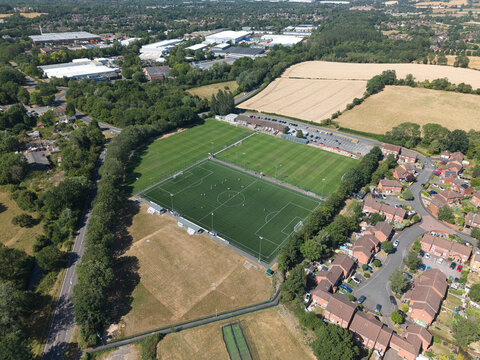 Aerial view of a football pitch surrounded by lush trees, residential housing, and green fields in Studley, England, United Kingdom.