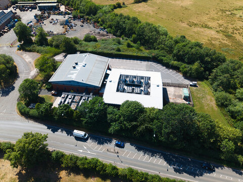 Aerial view of Six Degrees Data Centre featuring industrial HVAC cooling ventilation systems on the roof, surrounded by lush trees and a nearby road in Studley, England, United Kingdom.