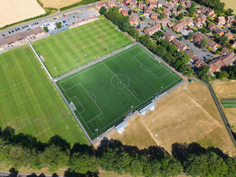 Aerial view of a football pitch surrounded by residential houses and green fields in Studley, England, United Kingdom.