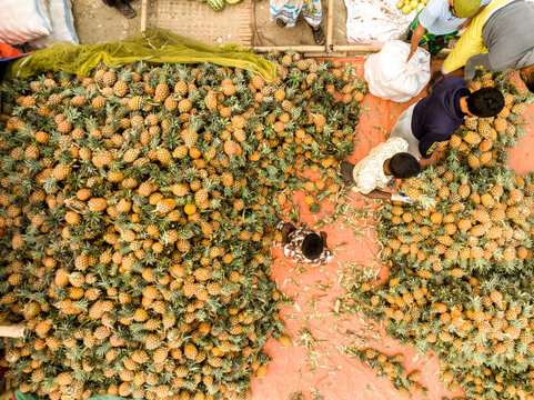 Dhaka, Bangladesh - 06 March 2026: Aerial view of Hazaribag market with workers sorting a massive pile of fresh pineapples on a red tarp.