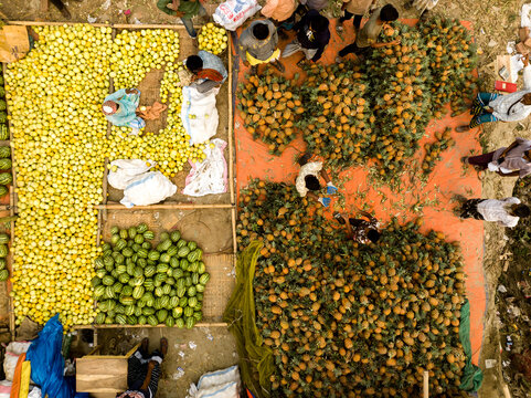 Dhaka, Dhaka Division, Bangladesh - 06 March 2026: Aerial view of Hazaribag market featuring vendors sorting large piles of pineapples, watermelons, and lemons on colorful tarps.