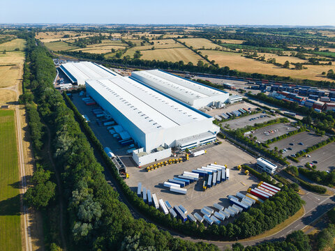 Aerial view of Daventry International Rail Freight Terminal with large white warehouses, distribution centers, and rows of parked HGVs and trailers in Kilsby, England, United Kingdom.