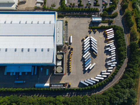 Aerial view of Daventry International Rail Freight Terminal featuring a large logistics warehouse and rows of parked heavy goods vehicles in the distribution yard in Kilsby, England, United Kingdom.