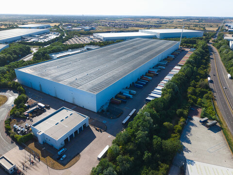 Aerial view of the Daventry International Rail Freight Terminal featuring large distribution warehouses with rows of parked HGVs at loading bays in Kilsby, England, United Kingdom.