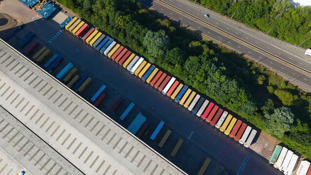 Aerial view of Daventry International Rail Freight Terminal showing rows of colorful shipping containers parked beside a warehouse near a highway in Kilsby, England, United Kingdom.