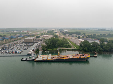 Buffalo, New York, United States - 15 July 2026: Aerial view of Vane Brothers tugboat and barge refueling on the Niagara River with a nearby marina and fuel tanks in the background under a hazy sky.