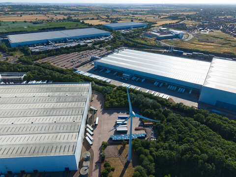 Aerial view of Daventry International Rail Freight Terminal featuring large warehouses, distribution centers, and parked HGVs with a wind turbine, Kilsby, England, United Kingdom.