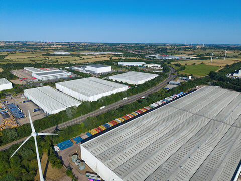 Aerial view of Daventry International Rail Freight Terminal featuring large warehouses, distribution centers, shipping containers, and wind turbines in Kilsby, England, United Kingdom.