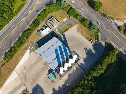 Aerial view of the Gasrec Bio-LNG refueling station at DIRFT, featuring white storage tanks, a service building, and paved forecourt, located near a road in Kilsby, England, United Kingdom.
