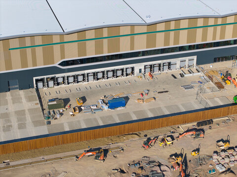 Aerial view of the Daventry International Rail Freight Terminal featuring a large distribution warehouse with loading docks and construction machinery in Kilsby, England, United Kingdom.