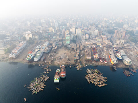 Dhaka, Bangladesh - 20 February 2026: Aerial view of Sadarghat river port with clustered wooden boats, cargo ships docked at the bank, and the dense urban cityscape under a hazy sky.