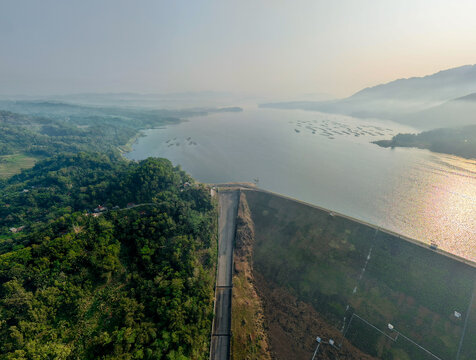 Aerial view of Wadaslintang Reservoir surrounded by lush green hills and calm water under a hazy sky in Wadaslintang, Central Java, Indonesia.