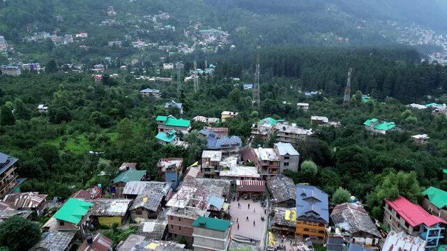 Aerial view of Manali town with colorful rooftops, lush green trees, and surrounding mountains in the Himalayas, Manali, Himachal Pradesh, India.