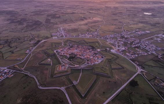 Aerial view of the historic star-shaped fortress with its surrounding stone walls, terracotta rooftops, and rural landscape at sunset in Almeida, Guarda District, Portugal.