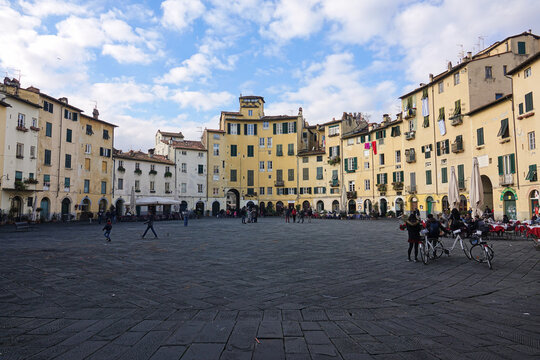 View of the historic Piazza dell'Anfiteatro, with its unique elliptical shape, yellow buildings, and cobblestone ground, Lucca, Tuscany, Italy.