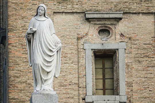 View of a stone statue of a nun standing in front of a historic brick building with a stone-framed window in Parma, Emilia-Romagna, Italy.