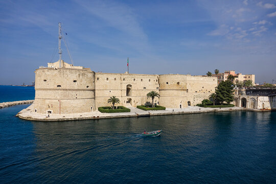 View of the historic Castello Aragonese fortress surrounded by blue sea with a small boat passing by in Taranto, Apulia, Italy.