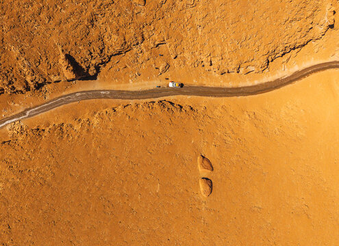 Aerial view of Canion de las Vizcachas featuring a winding dirt road through the arid orange landscape with a vehicle parked on the side in Nor Lipez, Potosi, Bolivia.