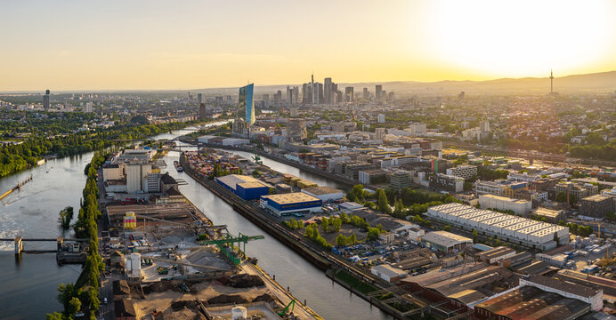 Aerial view of the Osthafen industrial harbor area along the Main river with the ECB and Frankfurt city skyline in the background during sunset in Frankfurt am Main, Hessen, Germany.