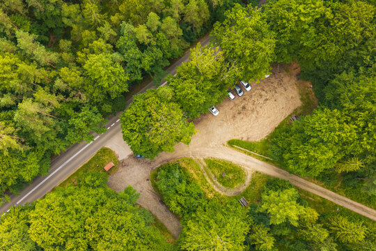 Aerial view of a forest clearing with a small parking area, several parked cars, and a winding road surrounded by dense green trees in Koleczkowo, Pomeranian Voivodeship, Poland.