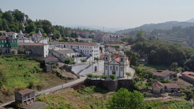 Aerial view of the Santuario de Nossa Senhora de Porto de Ave surrounded by historic buildings, lush green hills, and rural landscape in Taide, Braga, Portugal.