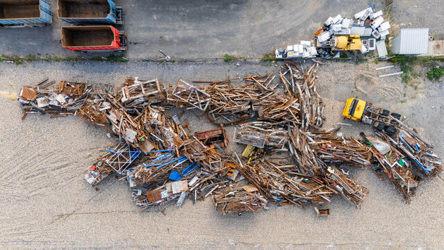 Aerial view of a scrap metal yard featuring large piles of rusted metal, a yellow truck, and industrial containers in Sremska Mitrovica, Vojvodina, Serbia.