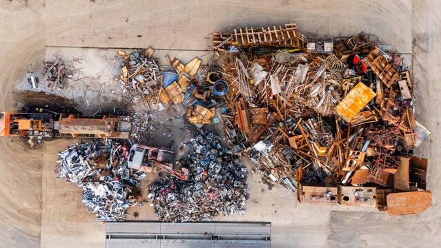 Aerial view of a scrap metal recycling yard featuring large piles of industrial waste, rusted metal components, and heavy machinery in Sremska Mitrovica, Vojvodina, Serbia.