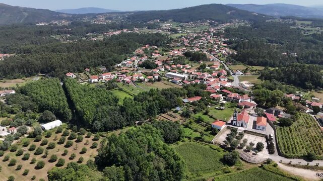 Aerial view of Igreja Paroquial de Freixo surrounded by green hills and agricultural fields in Freixo, Viana do Castelo, Portugal.