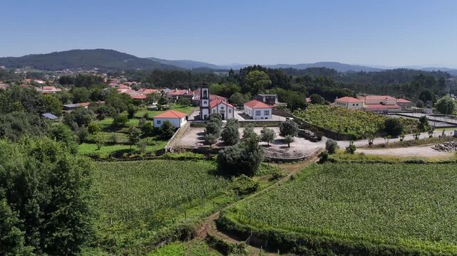 Aerial view of Igreja Paroquial de Freixo surrounded by lush vineyards and rolling hills in the rural landscape of Freixo, Viana do Castelo, Portugal.