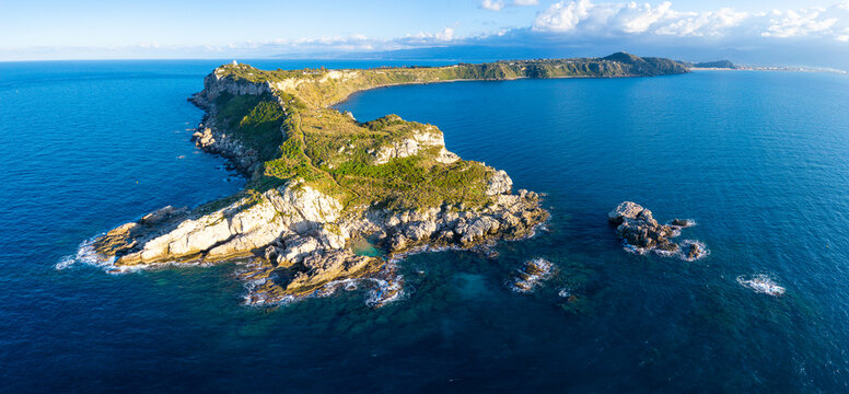 Aerial view of the Capo Milazzo peninsula, featuring rugged cliffs, coastal vegetation, and the surrounding Tyrrhenian Sea in Milazzo, Sicilia, Italy.