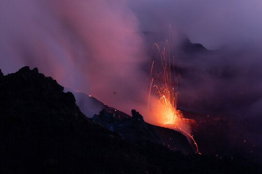 View of Stromboli erupting at night with glowing lava fountains and volcanic ash clouds rising into the dark sky in Lipari, Sicily, Italy.