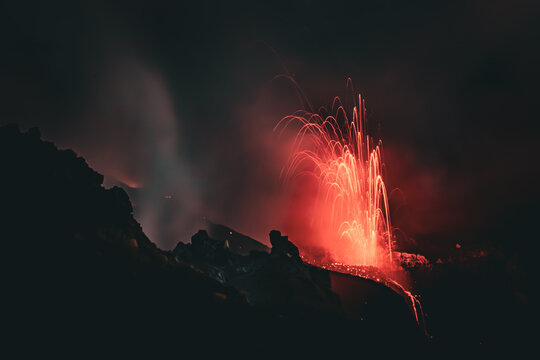 View of Stromboli erupting at night with glowing lava fountains and volcanic ash plumes rising into the dark sky in Lipari, Sicily, Italy.