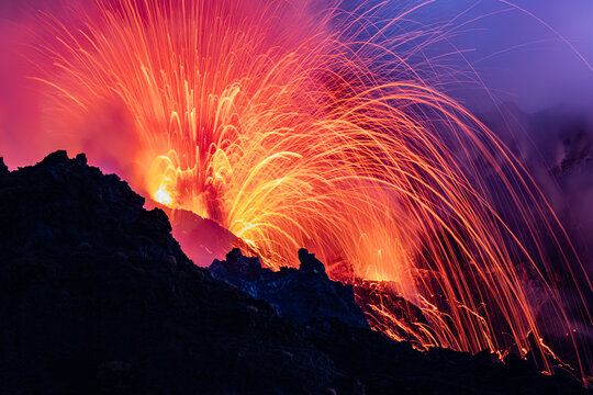 View of Stromboli erupting at night with glowing lava and sparks illuminating the dark volcanic landscape in Lipari, Sicily, Italy.