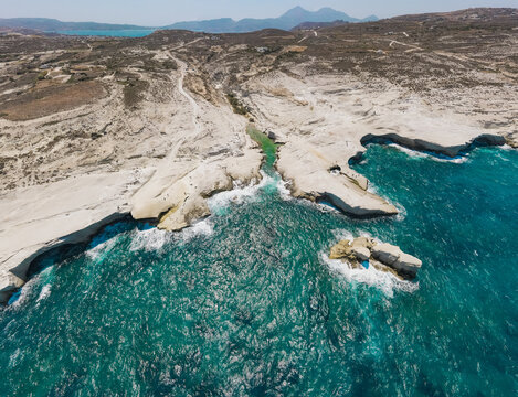 Aerial view of the volcanic white rock formations of Sarakiniko Beach meeting the turquoise Aegean Sea on the island of Milos, Greece.