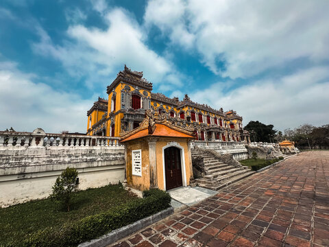 Hue, Hue, Vietnam - 06 February 2026: View of the historic Imperial City, featuring ornate yellow architecture, intricate stone carvings, and a tiled courtyard under a cloudy sky.