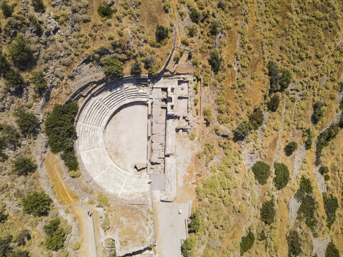 Aerial view of the Ancient Theater of Milos, a well-preserved Roman-era amphitheater nestled in a rugged hillside with stone seating and surrounding dry vegetation in Milos, Greece.