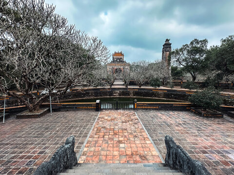 Hue, Hue, Vietnam - 06 February 2026: View of the historic Minh Mang Tomb with its traditional stone architecture, reflecting pond, and bare trees under a cloudy sky.