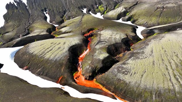 Aerial view of the vibrant red river flowing through the volcanic landscape of Raudufossafjoll with patches of snow and mossy terrain in Hella, Rangarthing ytra, Iceland.