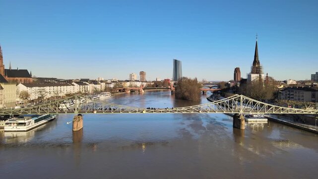 Aerial view of the historic Eiserner Steg footbridge spanning the Main River with the city skyline and boats in Frankfurt am Main, Hessen, Germany.