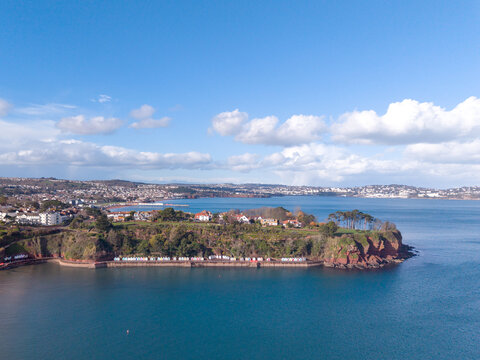 Aerial view of the coastal headland at Paignton featuring colorful beach huts, lush green parkland, and the town skyline overlooking the sea in Paignton, England, United Kingdom.