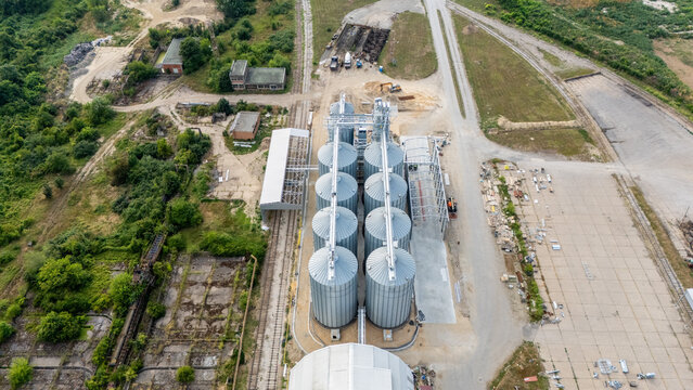 Aerial view of industrial grain silos with metal storage tanks, railway tracks, and surrounding rural landscape in Sremska Mitrovica, Vojvodina, Serbia.
