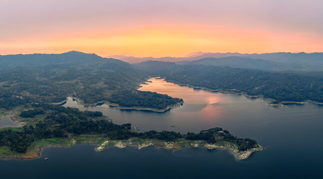 Aerial view of Wadaslintang Reservoir surrounded by lush green hills under a warm sunset sky in Wadaslintang, Central Java, Indonesia.