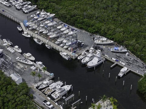 Islamorada, United States - 23 June 2026: Aerial view of a marina in Florida featuring numerous motorboats docked in slips and stored on multi-level racks near dense mangroves.