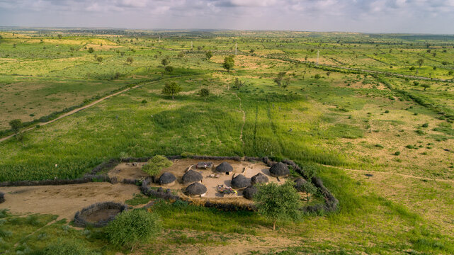 Aerial view of a traditional rural settlement with thatched huts surrounded by a fenced enclosure in the green landscape of Nagarparkar, Sindh, Pakistan.