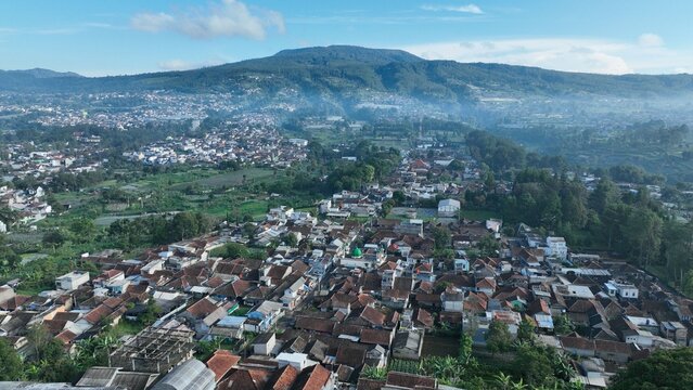 Aerial view of the town of Lembang nestled among lush green hills and mountains with dense residential rooftops under a clear sky in Lembang, West Java, Indonesia.