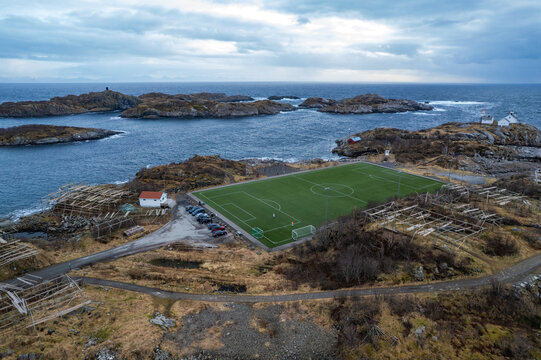 Aerial view of a football pitch located on a rocky island surrounded by the sea and traditional wooden fish drying racks in Skaland, Lofoten, Norway.