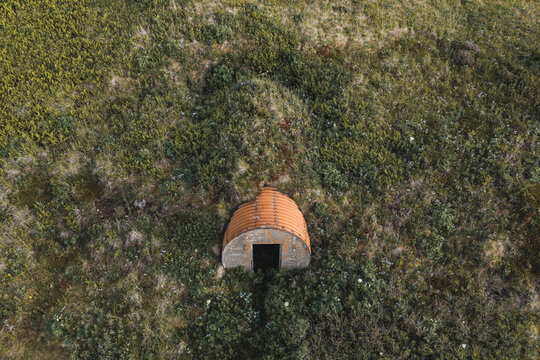 Aerial view of a historic orange Quonset hut nestled in the grassy hills of Unalaska, Alaska, United States.