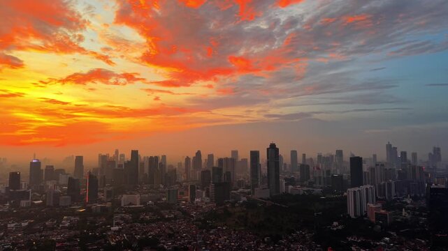 Aerial view of the vibrant Jakarta skyline illuminated by a dramatic orange sunset, showcasing urban architecture and high-rise buildings in Tebet, Jakarta, Indonesia.