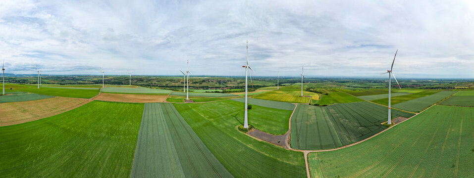 Aerial view of wind turbines standing in vast green agricultural fields under a cloudy sky in Worms, Rhineland-Palatinate, Germany.